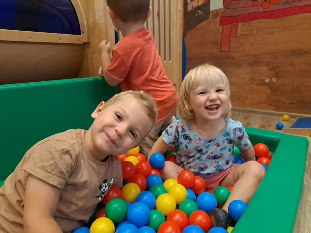 Dwoje uśmiechniętych dzieci w suchym basenie z kolorowymi piłeczkami